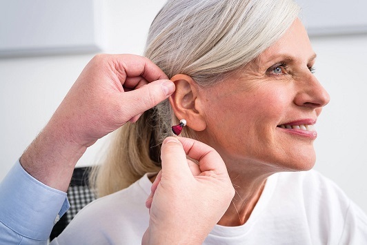 Ältere Frau bekommt ein Hörgerät angepasst, Hörakustiker hilft beim Einsetzen des Geräts.